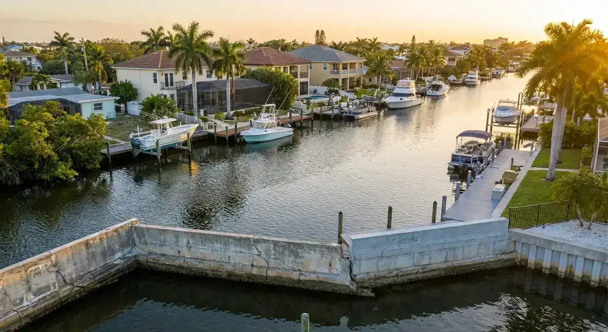 Aerial view at sunset of an aging cracked concrete seawall along a residential canal with docks