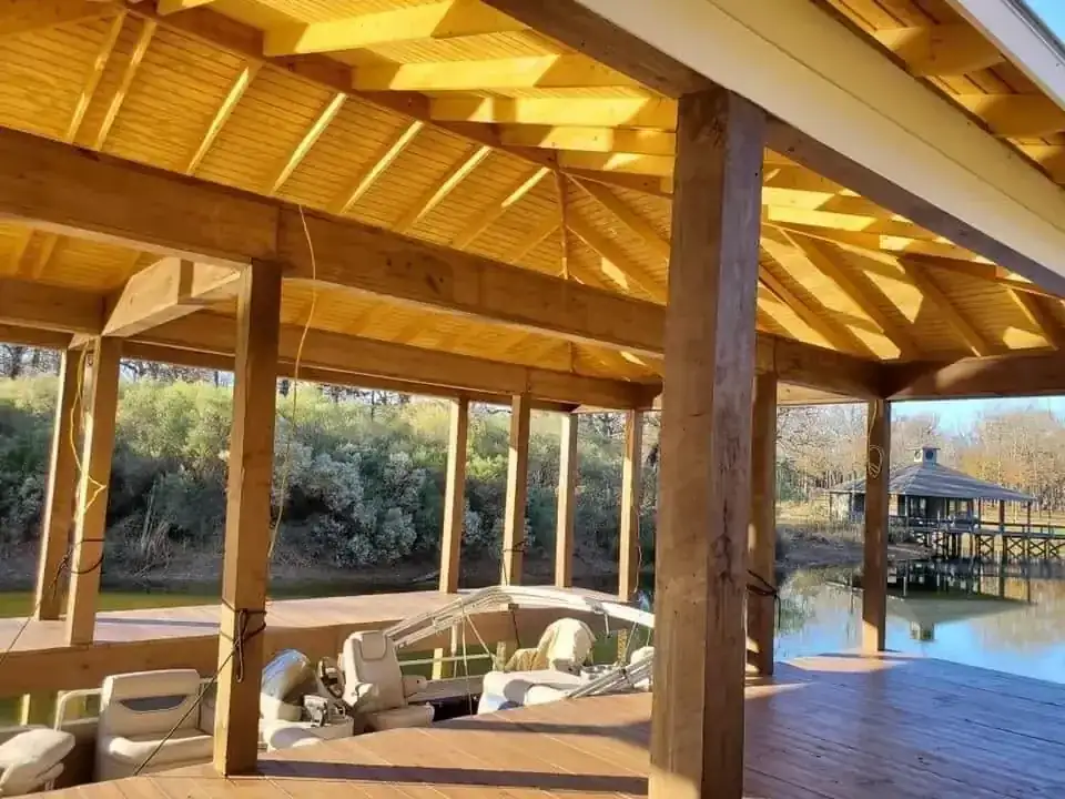 Covered wood boathouse dock with exposed rafters sheltering a pontoon boat on a lake